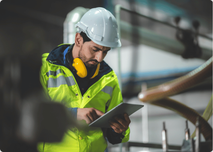 Safety professional in hard hat and high-visibility vest conducting site inspection with tablet