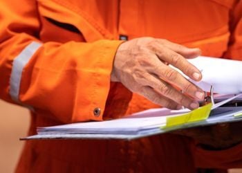 Safety auditor in high-visibility vest reviewing compliance documentation and safety records