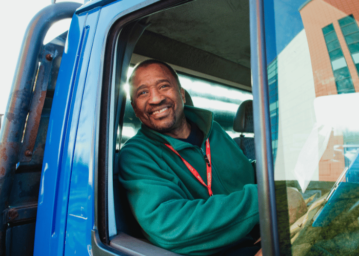Professional truck driver in safety vest smiling from cab of commercial transport vehicle