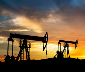 Oil drilling rigs silhouetted against sunset sky in oil and gas field