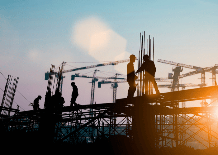 Construction workers in safety gear working on steel framework at sunrise