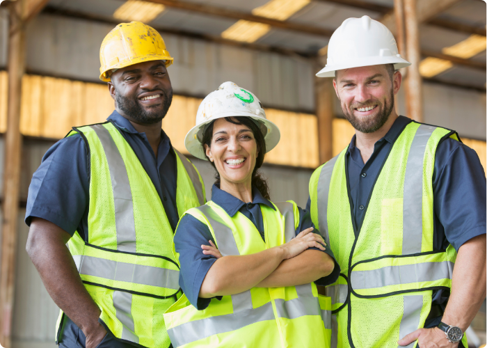 Diverse team of safety professionals in hard hats and safety vests smiling at construction worksite