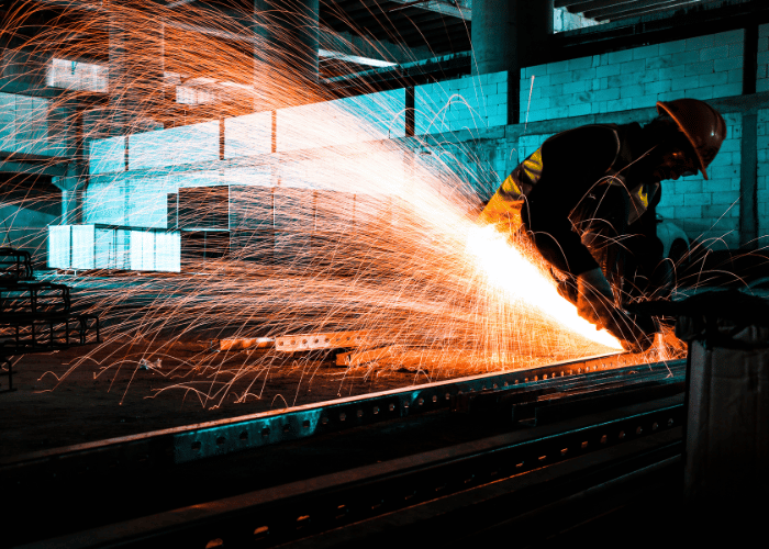 Industrial manufacturing worker operating equipment with safety sparks and protective gear